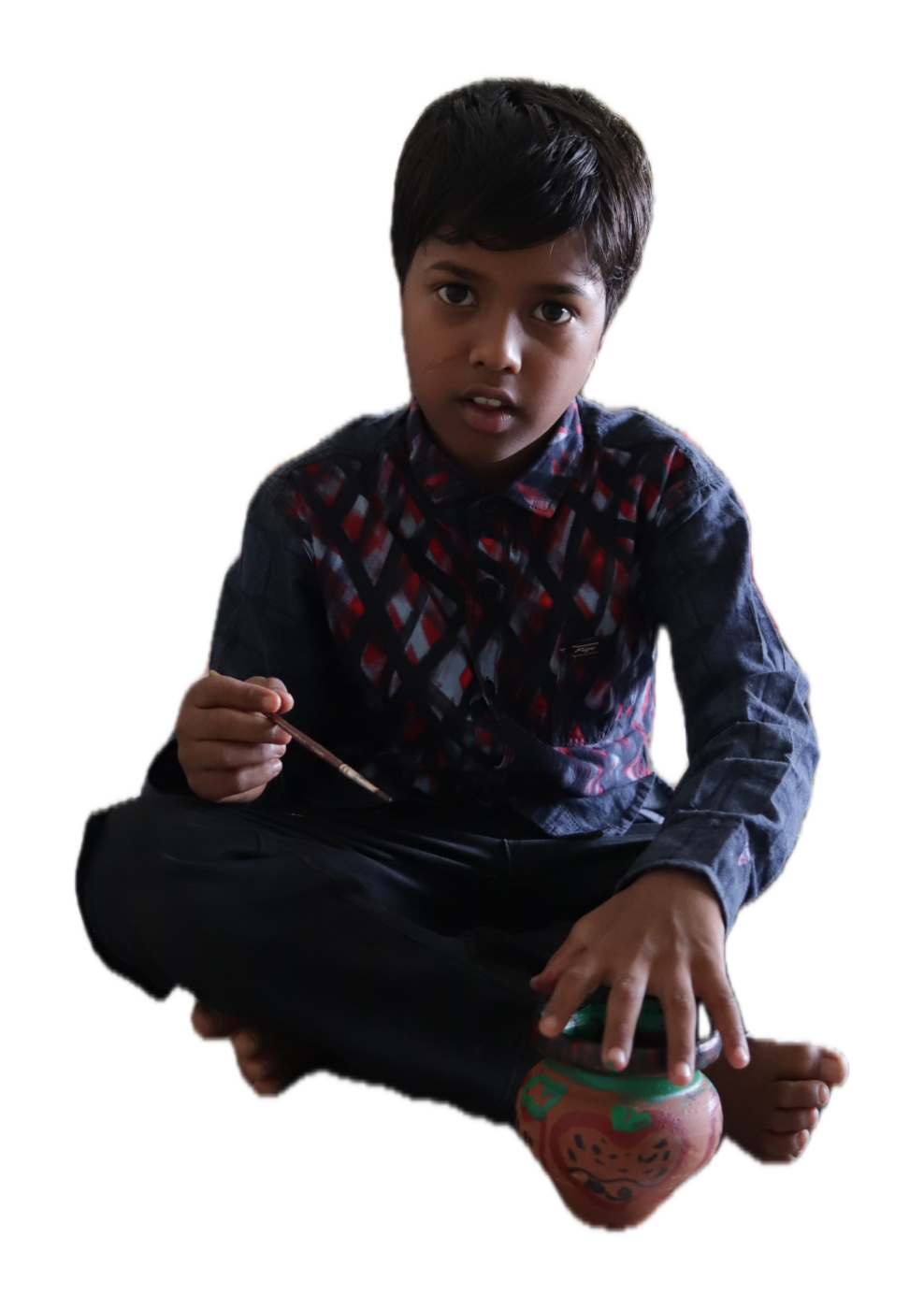 A boy sitting cross-legged beside the pot he is painting